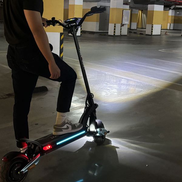 Jezdec stojí na osvětlené elektrické koloběžce v podzemním parkovišti.